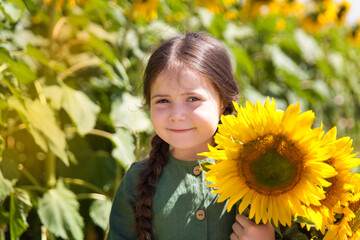 Naklejka premium Funny small girl in a field of sunflowers