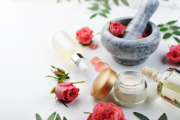 Handmade rose cosmetics concept of mortar and pestle with rose buds with dropper and bottles with serum and oil on white background