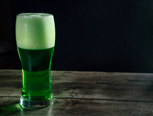Glass of green beer on wooden bar counter against dark background, concept for st patrick's day