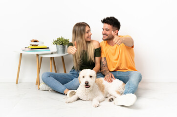 Young caucasian couple with dog staying at home giving a thumbs up gesture
