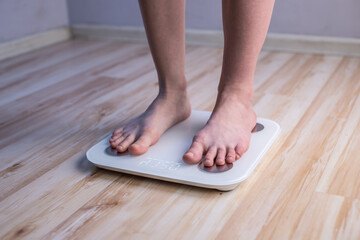 Women's bare feet stand on electronic scales on the wooden floor. Concept of fitness and weight loss tracking