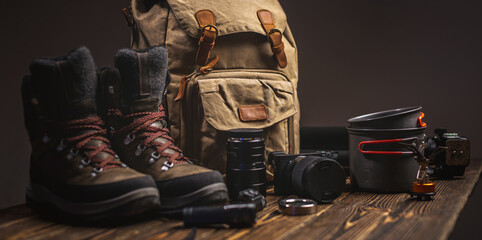Hiking equipment for a tourist on vacation. Backpack camera, and boots on a wooden table. Concept of an active lifestyle - 413239666