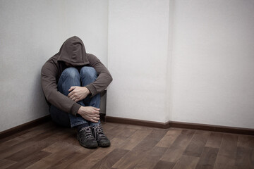 desperate young drug addict wearing hood and sitting alone in corner