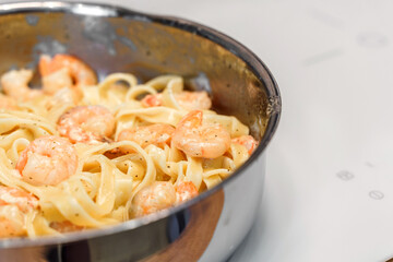 Hot creamy pasta with shrimp is cooked on the stove in a frying pan