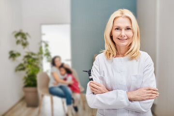 Female audiologist with otoscope in hands standing over background her patients in a hearing clinic