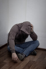 Fototapeta premium desperate young drug addict wearing hood and sitting alone in corner