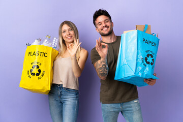 Young caucasian couple recycling isolated on purple background showing an ok sign with fingers