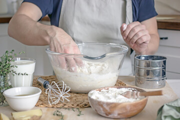 A faceless man in an apron in his kitchen at the kitchen table kneads bread dough in a glass bowl with his hands. Home authentic hobby, home baker. Baking bread with your own hands