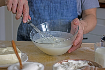 A man without a face in an apron holds a whisk in his hands and kneads dough for baking in the kitchen. Authentic home cooking hobby, home baker. Man cooking in the kitchen at home