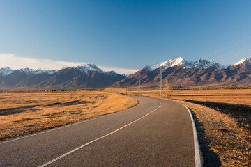A long road leading to a large snow capped Sayan mountain on a sunny day