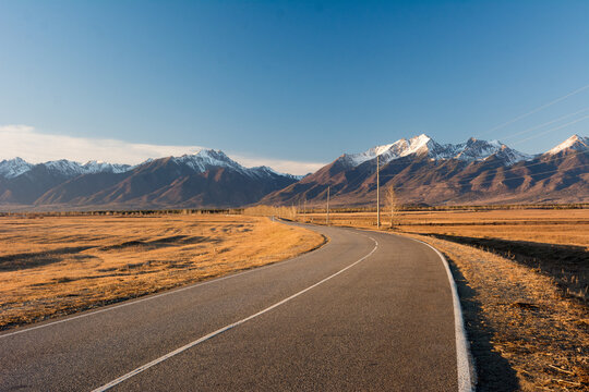 A long road leading to a large snow capped Sayan mountain on a sunny day