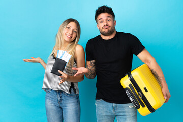 Young caucasian couple going to travel isolated on blue background having doubts while raising hands and shoulders