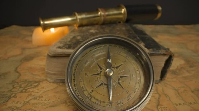 The telescope on top of the thick book and the compass on top of the navigational map