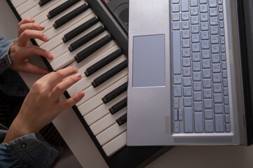 Fototapeta na wymiar Close-up of female hands on the electric piano. A woman is learning to play the synthesizer on a laptop