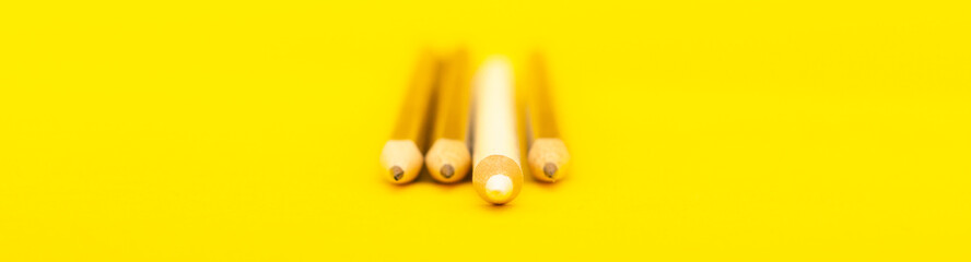 A white pencil that stands out from the crowd of many identical black counterparts on a yellow background. Leadership, uniqueness, independence, initiative, strategy, dissent, business success concept