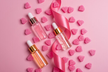Obraz na płótnie Canvas Skin care essence glass bottles on pink background with heart shape decorations and ribbon. Hydrating anti aging serum, collagen and peptides, bottle with dropper. Cosmetics, shopping and spa concept