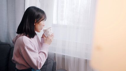 Young lonely asian woman drinking morning coffee and looking through the window. High quality photo