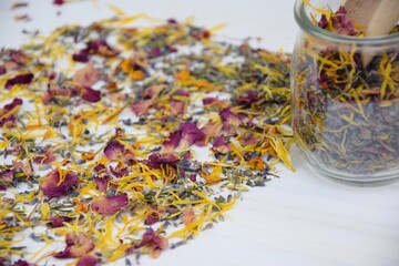 Colorful fragrant herbs on glass jar and on white wooden background, preparing bath salt