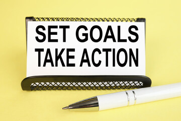 Set Goals, Take Action. text on white paper on a yellow background near the pen.