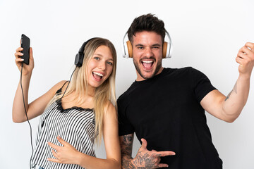 Young caucasian couple on white background listening music and doing guitar gesture