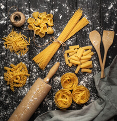 Surtido de pasta italiana sin cocer sobre madera rústica negra con harina y un rodillo de amasar.