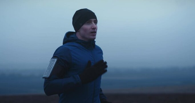Close up shot of young handsome man in sportswear running fast outdoors on foggy morning. Test of human endurance.