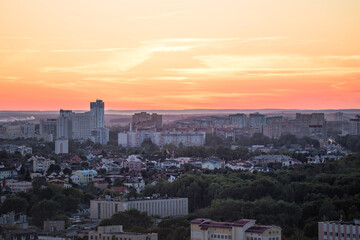 Panorama of a big city from a great height at sunset. View of the city of Minsk. Colorful red sky, many different houses and green trees on the streets of the city.