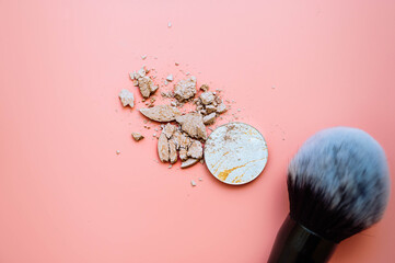 Makeup brush and crushed powder highlighter bronzer on pink background. Top view.