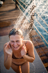 Beautiful young woman takes a relaxing shower in a swimsuit on a sunny day outdoors by the sea. The girl on vacation is resting. Selective focus