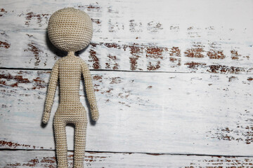 faceless knitted human figure on wooden background close up