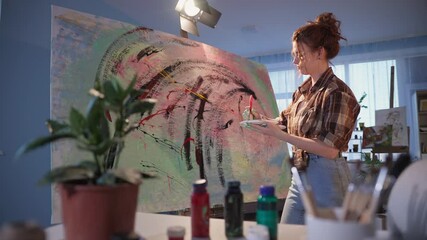 creative artist actively uses a brush while creating a painting on large canvas, stylish girl during a hobby in studio