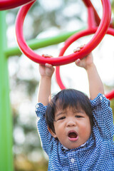 Fototapeta na wymiar Happy asian child boy climb on playground bar in city park
