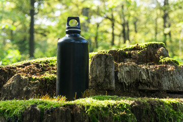 A metal flask for water stands on an old tree stump in the forest. Eco friendly, camping and healthy lifestile concept.