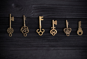 set of antique copper keys lie in a row on a black wooden background. Decorative keys pendants. The...