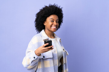 Young African American woman using mobile phone isolated on purple background with happy expression