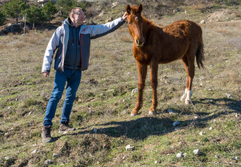 An elderly tourist gently strokes a randomly encountered wild foal in the mountains