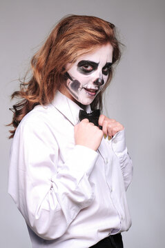 girl in Halloween makeup in the image of a dead man with a white-black skull in a plain shirt with a bow tie