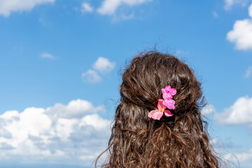 A turned-back girl with pink flowers in her hair looks out at the landscape against a beautiful...