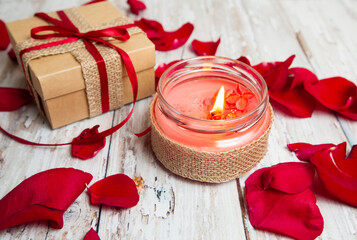 romantic background with burning candle, gift box and rose petals on a wooden table. shallow depth of field