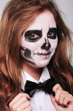 girl in Halloween makeup in the image of a dead man with a white-black skull in a plain shirt with a bow tie