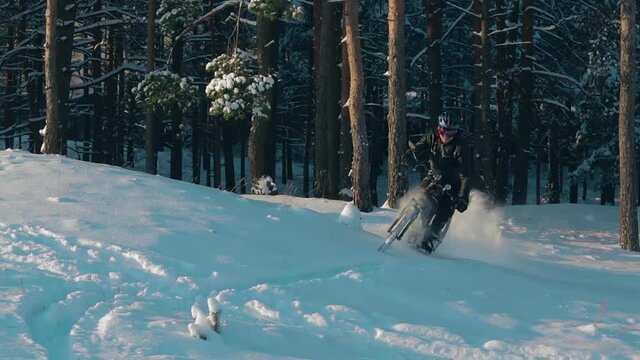 Cyclist in Black Clothes, Helmet and Snow Glasses Riding on Electric Bike in the Snow in Winter Forest. E-Bike Riding and Drifting at Cold Sunny Day - Slow Motion