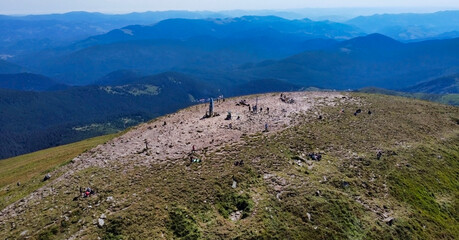 A view from a height to the highest mountain in Ukraine, Hoverla. People at the top and stele. Panorama of the mountains. Summer in Carpathians. Europe