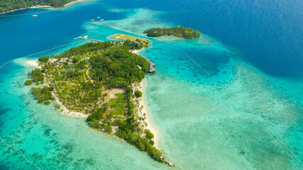 Aerial drone of Seascape with beautiful beach and tropical Malipano island with palm trees by coral reef from above. Philippines, Samal.