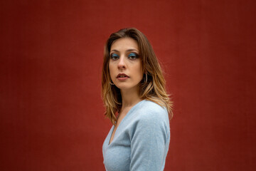 Portrait of a caucasian woman, model, looking at the camera, with an street red wall in the background. Fashion, editorial and model concept. Copyspace