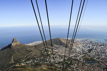 Fototapeta premium View of Cape Town from inside the cable car that takes people up to Table Mountain. The cables are in the foreground. The city, sea, Lion's Head in the background.