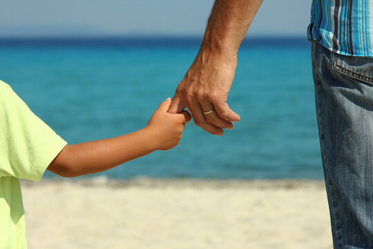 The parent holds the child's hand on the beach