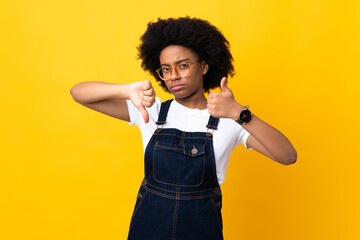 Young African American woman isolated on yellow background making good-bad sign. Undecided between yes or not