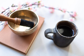 Singing bowl or Tibetan bowl on white blanket with cherry flower and cup drink, tea or coffee.