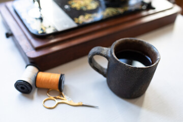 Tea time, coffee time, relaxation time along with vintage sewing machine, thread bobbins and antique scissor on white table.