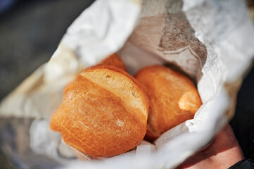 View into an open paper bag with fresh buns that is held in hands.